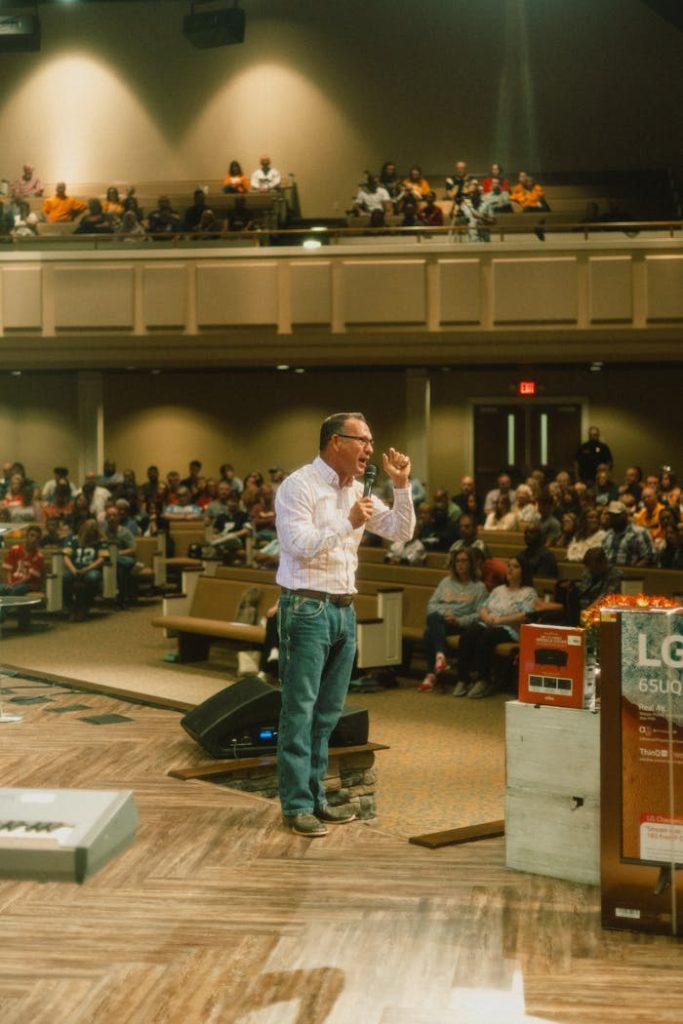A speaker engages with a diverse audience in a well-lit indoor venue.